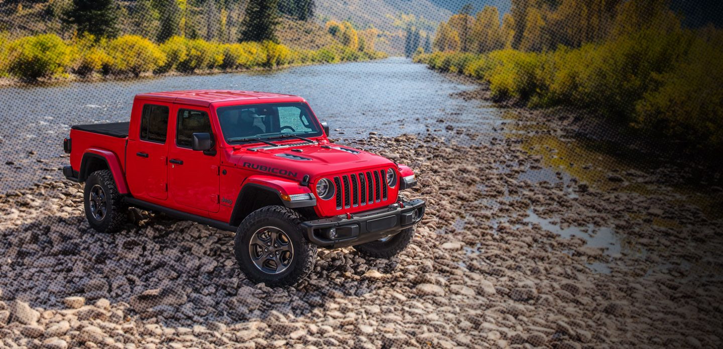 Red Gladiator parked beside a rocky stream