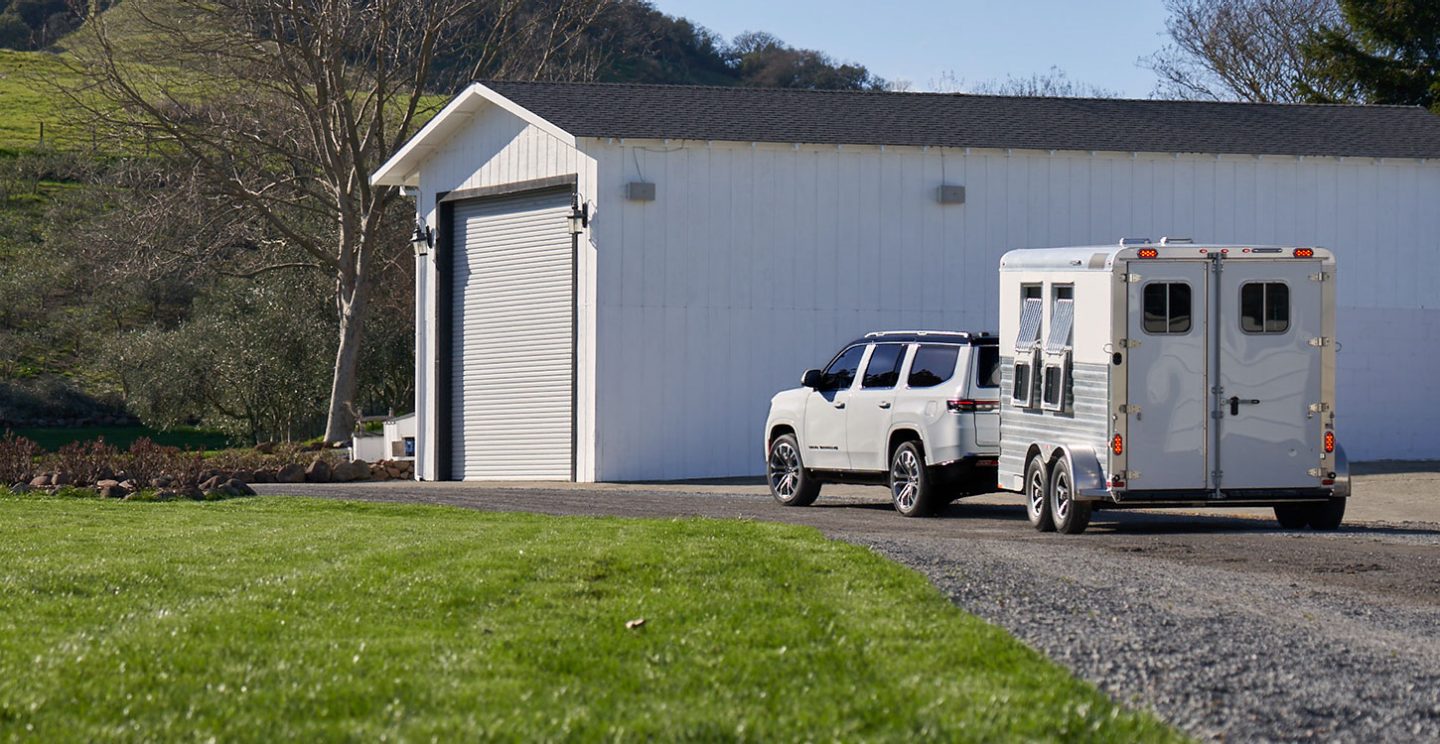 The 2022 Grand Wagoneer towing a horse trailer on a gravel drive.